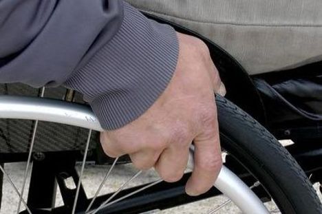 Die rechte Hand einer Person fasst an einen Reifen von einem Rollstuhl.